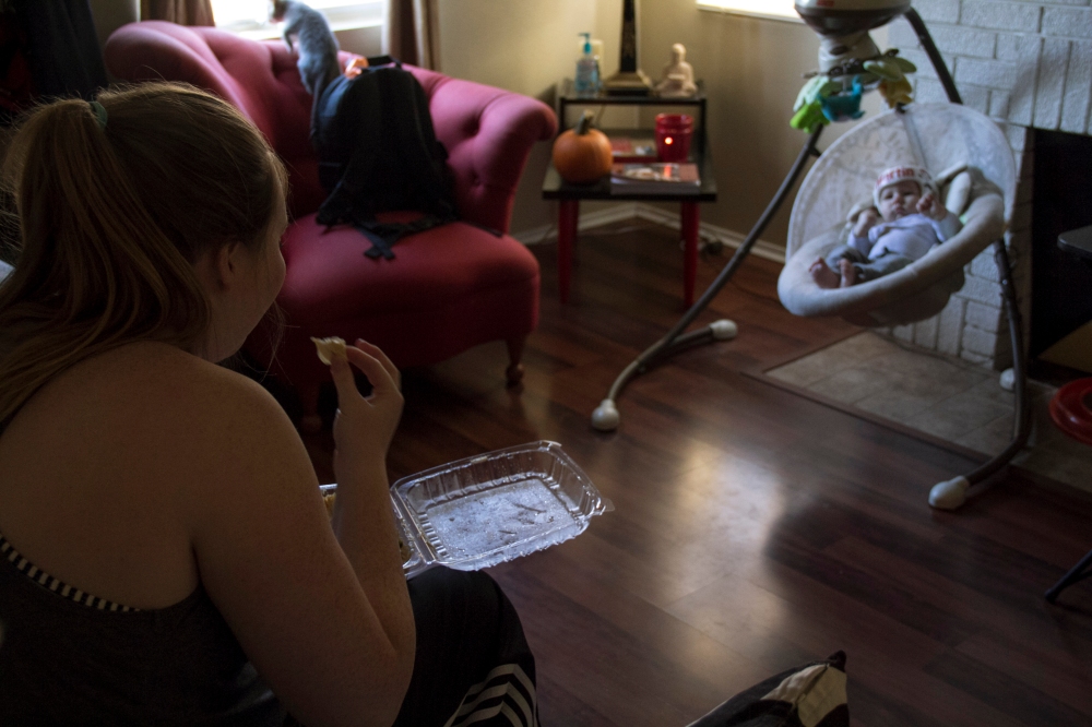 Chandler Ignatowicz eats while watching Martin Williams on Nov. 4, 2014 in their home. Chandler Ignatowicz doesn't have much time to herself and sets him in the rocker to eat. (Photo by Alexis Macklin)